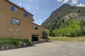 A two-story building with a garage entrance, surrounded by a rocky landscape and a forested mountain.