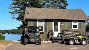 En liten stuga av trä med en brygga, en svart fyrhjuling och en gul golfbil parkerad framför.