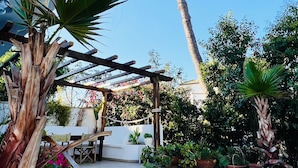 Ein überdachter Außenbereich mit Pergola, Topfpflanzen und einer Treppe zu einem Gebäude.