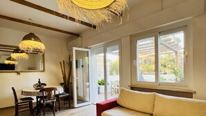Ein geräumiges Wohnzimmer mit Holzboden, einem roten Sofa, einem Esstisch mit Stühlen und einer großen, gewebten Pendelleuchte.