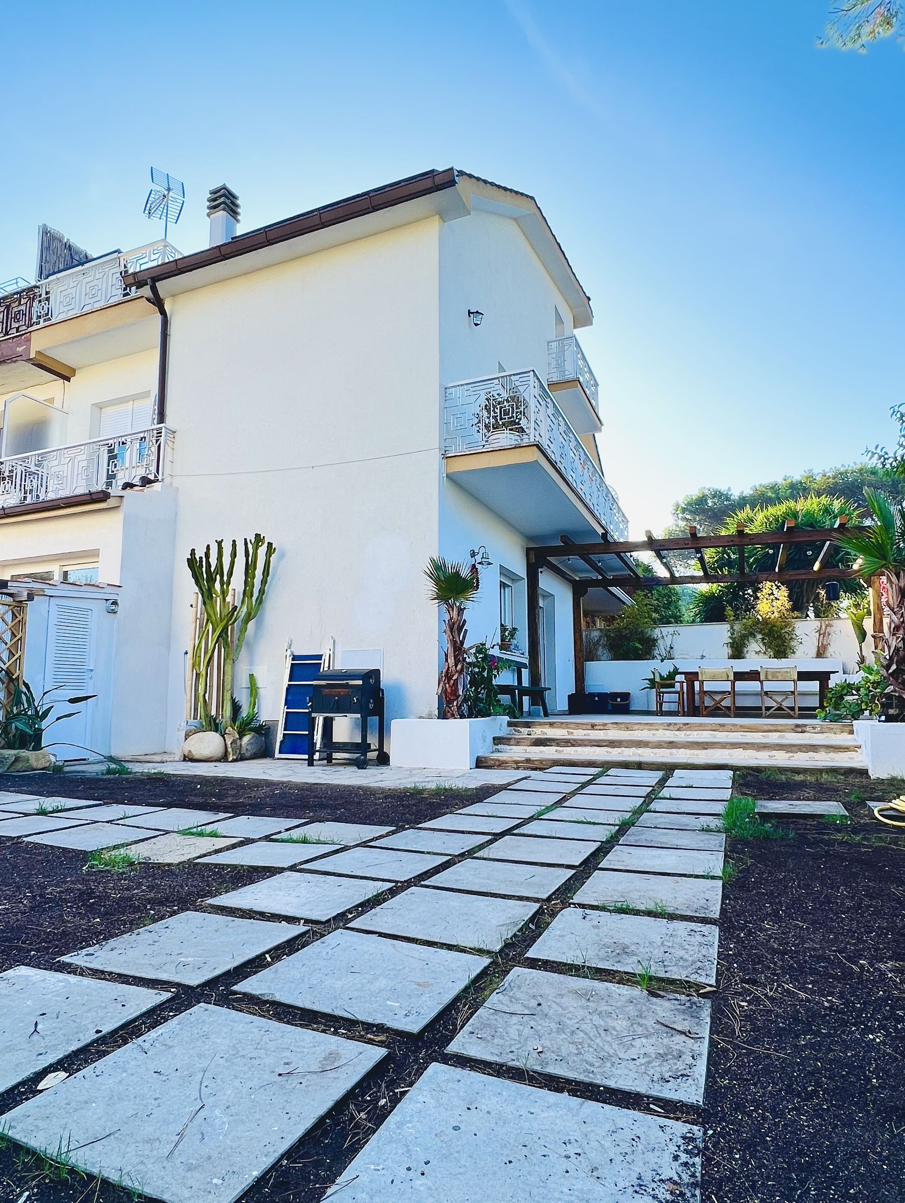 A modern building with a white facade, a covered outdoor seating area, and a stone pathway leading to the entrance.