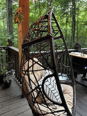 A wooden deck with a hanging chair, a table, and a grill.