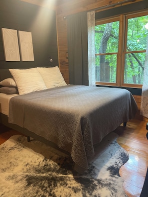 A bedroom with a bed, a window, and a view of trees.