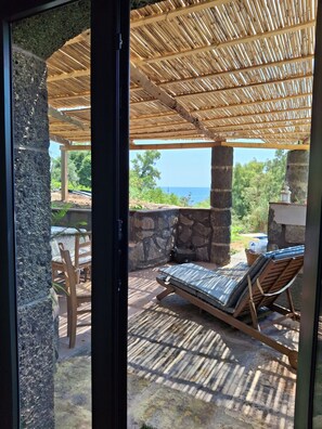 A covered outdoor seating area with a view of the sea, stone walls, and a wooden table with chairs. - typical Sicilian stone house on the sea surrounded by greenery (Riposto)