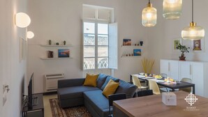 A modern living room with a sofa, a dining table, and pendant lights. - La Terrazza sull'Antico Mercato (Syracuse)