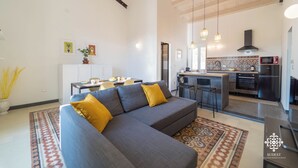 A modern living room with a grey sofa and yellow cushions, a dining area with a table and chairs, and a kitchen with a microwave and stove. - La Terrazza sull'Antico Mercato (Syracuse)