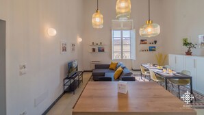 A modern living room with a sofa, dining table, and hanging pendant lights. - La Terrazza sull'Antico Mercato (Syracuse)