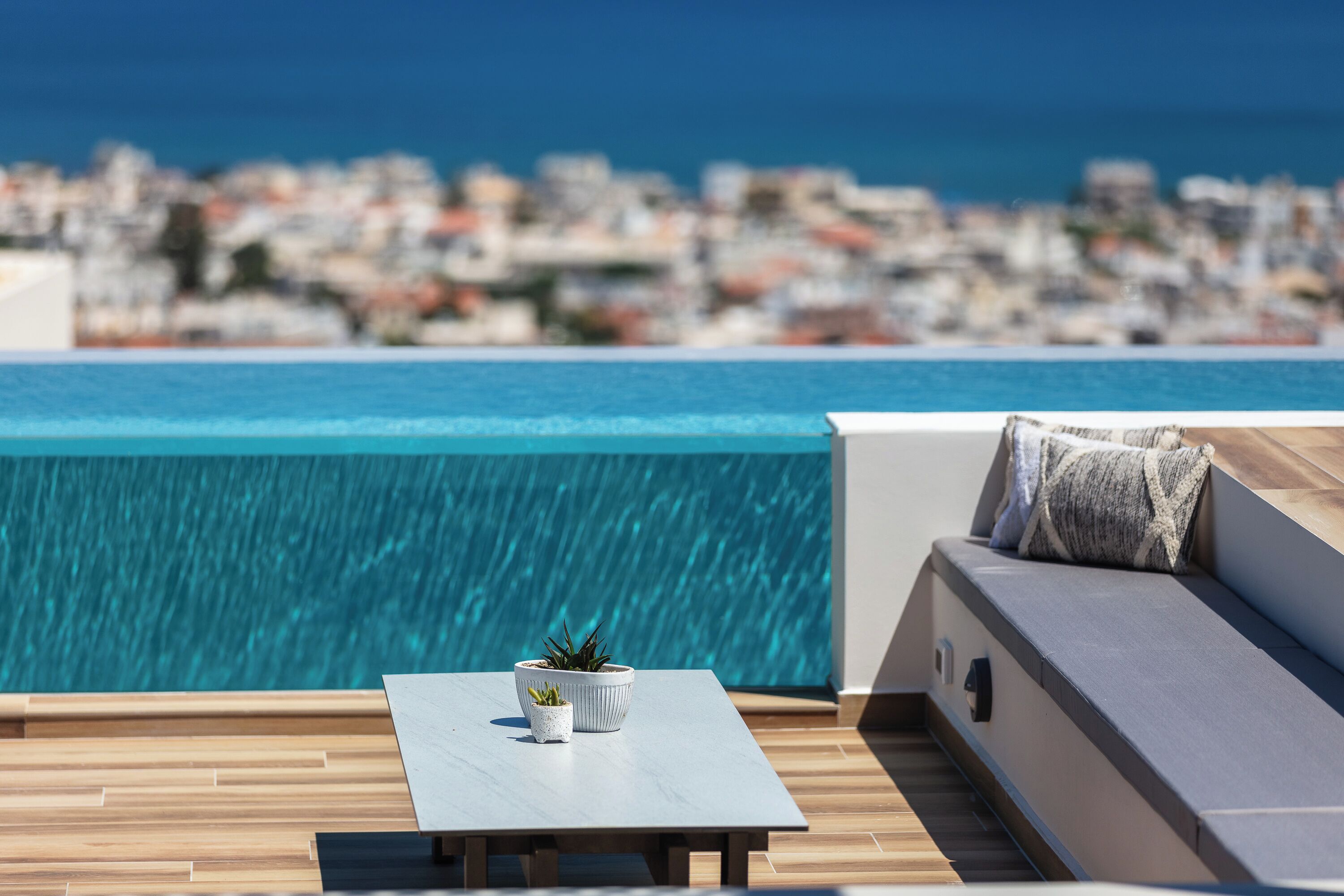 A rooftop terrace with a pool, a seating area with cushions, and two potted plants.