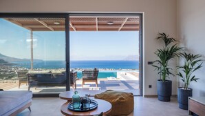 Ein modernes Wohnzimmer mit einer großen SchiebeglasTür, die auf einen Balkon mit Blick auf das Meer und die Berge führt.