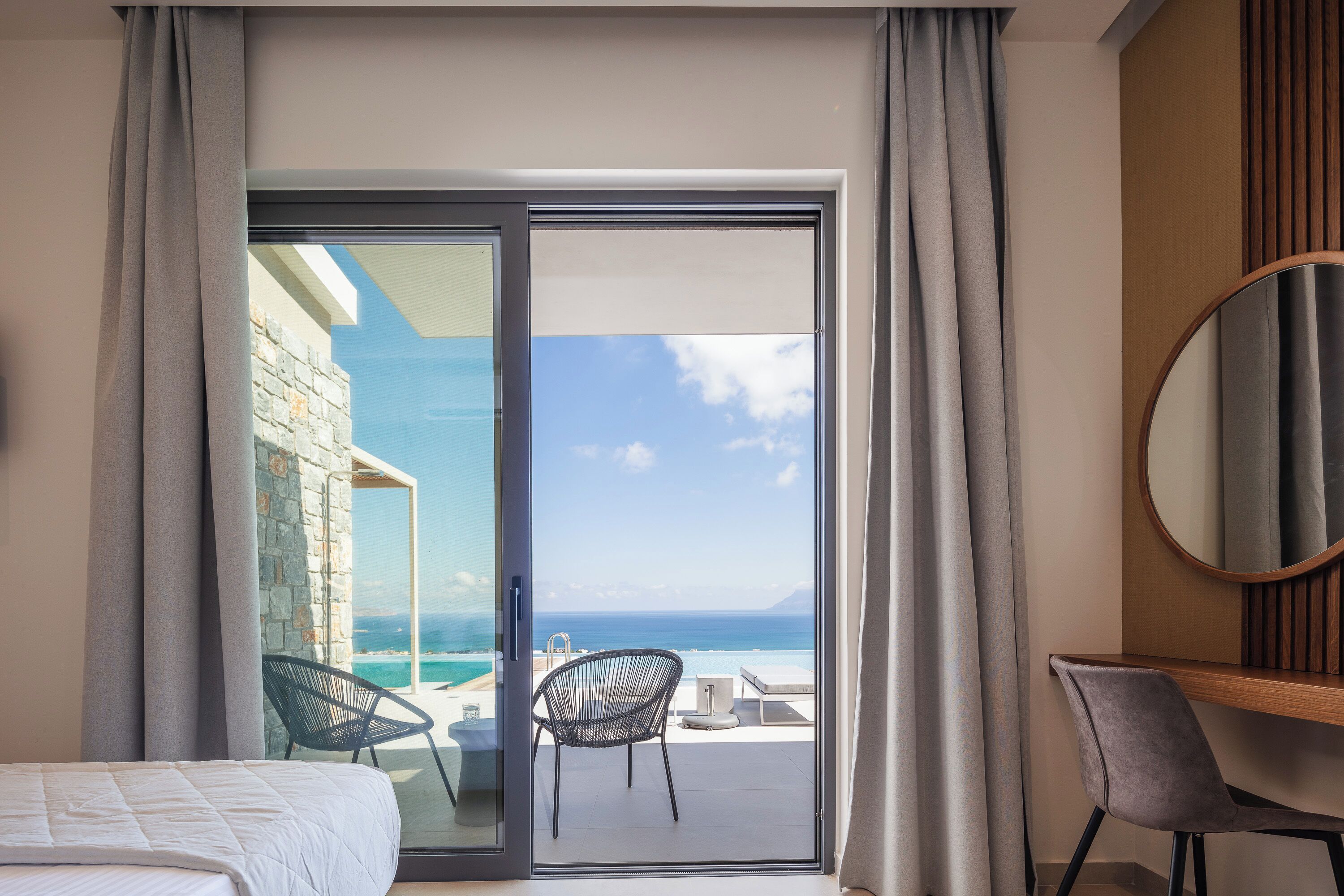 A hotel room with a bed, a desk, a chair, and a view of the ocean through a sliding door.