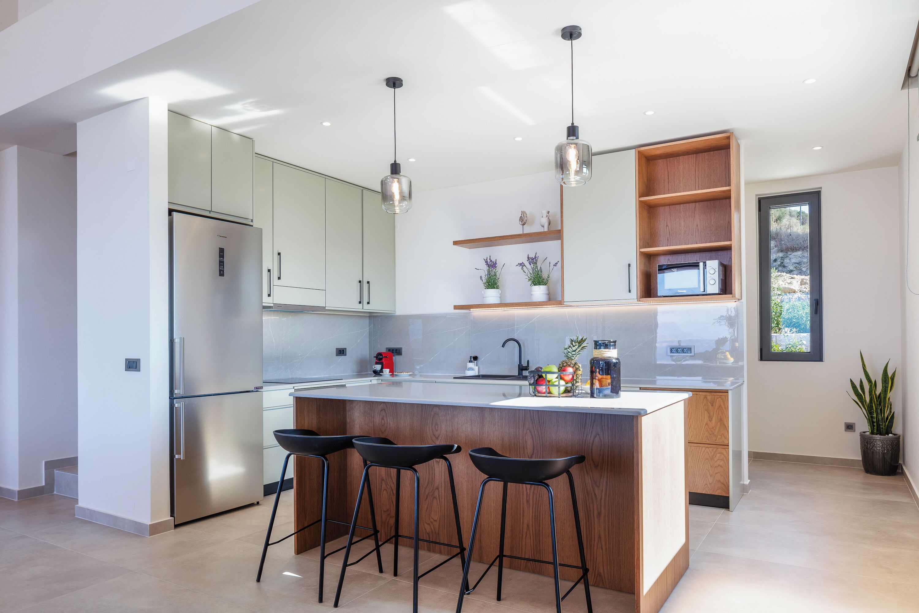 Une cuisine moderne dotée d’un îlot central, d’appareils électroménagers en acier inoxydable et de tabourets de bar.