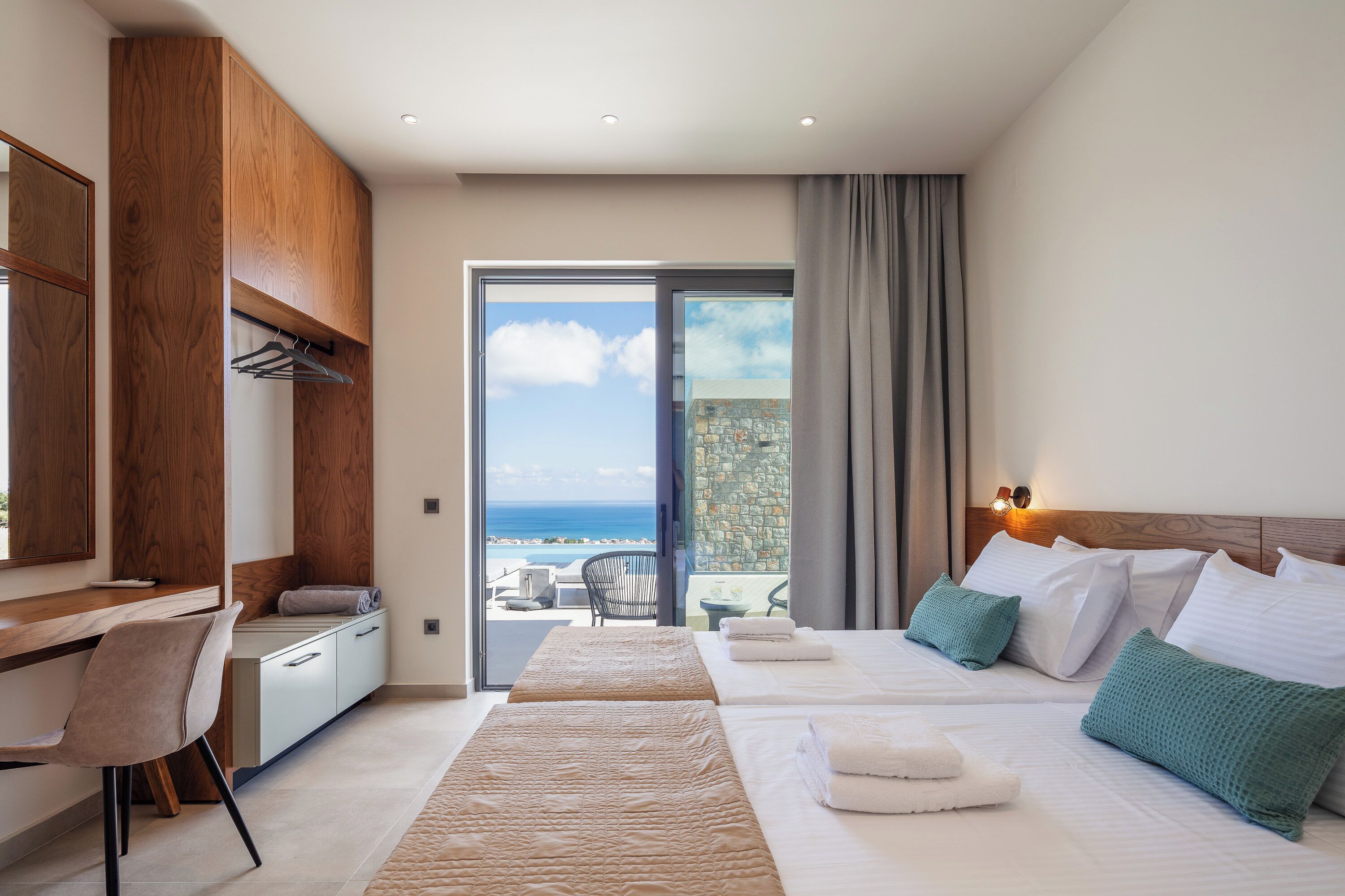 A hotel room with a desk, two beds, a view of the sea, and a balcony.