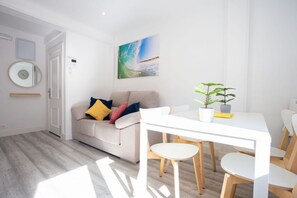 A modern living room with a white sofa, a dining table, and a potted plant.