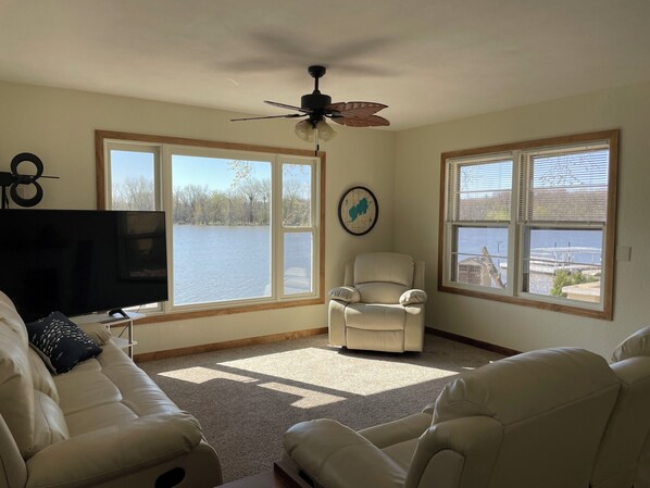 A living room with a large window, a ceiling fan, a TV, and a chair.