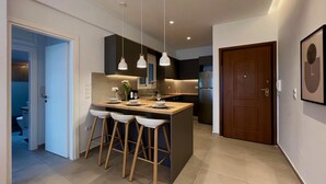 A modern kitchen with a central island, pendant lights, and a door leading to a bathroom. - AgiasFoteinis20  ·  Nea Smirni Square chic apartme (Athens)
