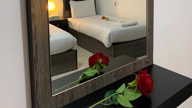 A hotel room with a bed, a bedside table, a mirror, and a red rose on the table.