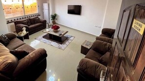 A living room with a large window, a flat-screen TV, and a 'Living Room' sign on the door.