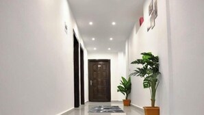 A hallway with a patterned carpet, potted plants, and a door at the end.
