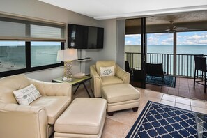 A living room with a beige sofa, two armchairs, and a TV on the wall.