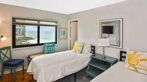 A bedroom with a bed, a desk, a chair, a window with a view of the beach, and a mirror on the wall. - SEA WINDS 1201  
Beach Front Getaway with spectacular views of the Gulf! (Marco Island)