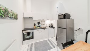 A compact kitchen with white cabinets, a black countertop, a microwave, a refrigerator, and a small dining table with a chair. - 3 Bedrooms - 72sqm - 15 Min. City Center (Vienna)