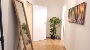 A hallway with wooden flooring, a potted plant, a painting on the wall, and a door. - 3 Bedrooms - 72sqm - 15 Min. City Center (Vienna)