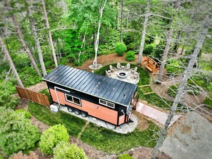 Eine kleine Holzhütte mit Metalldach, umgeben von einem Wald. Sie besitzt eine Feuerstelle und Sitzgelegenheiten im Freien.