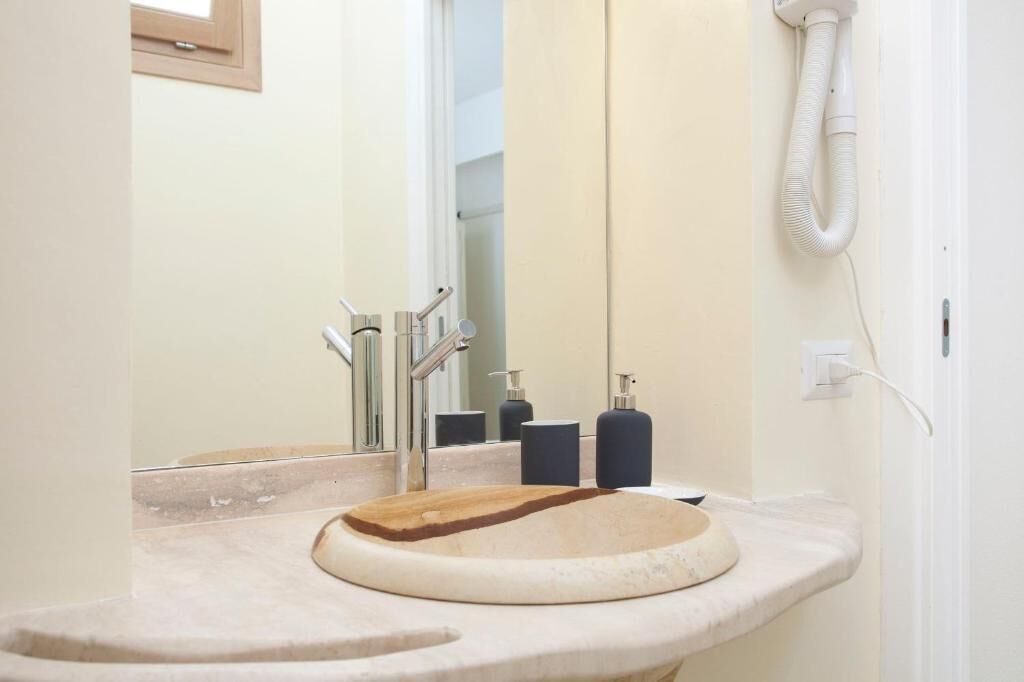 A bathroom with a round sink, a mirror, and a hairdryer on the wall.