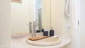 A bathroom with a round sink, a mirror, and a hairdryer on the wall.