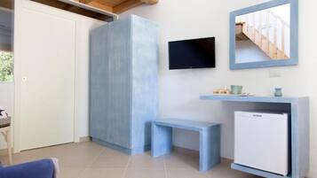A compact room with a white door, a blue cabinet, a small bench, a mounted TV, and a white mini-fridge.