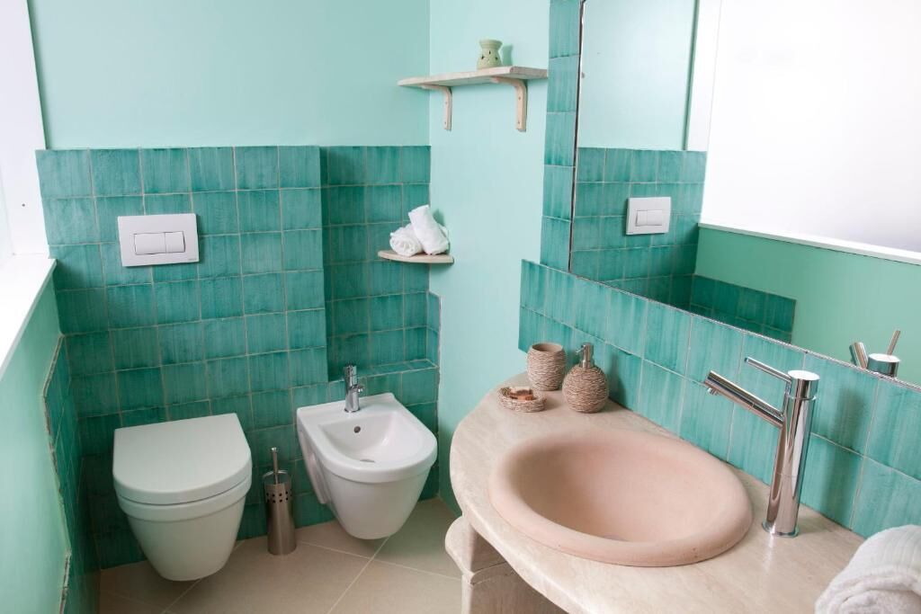 A bathroom with a toilet, bidet, and sink, with teal tiles and a mirror.
