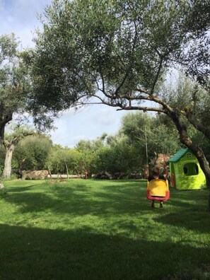 Relax in a serene outdoor setting with a charming swing and nearby playhouse amidst lush greenery.