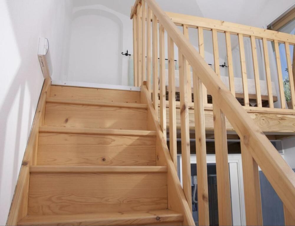 Een houten trap met een leuning, die naar een hogere verdieping leidt.