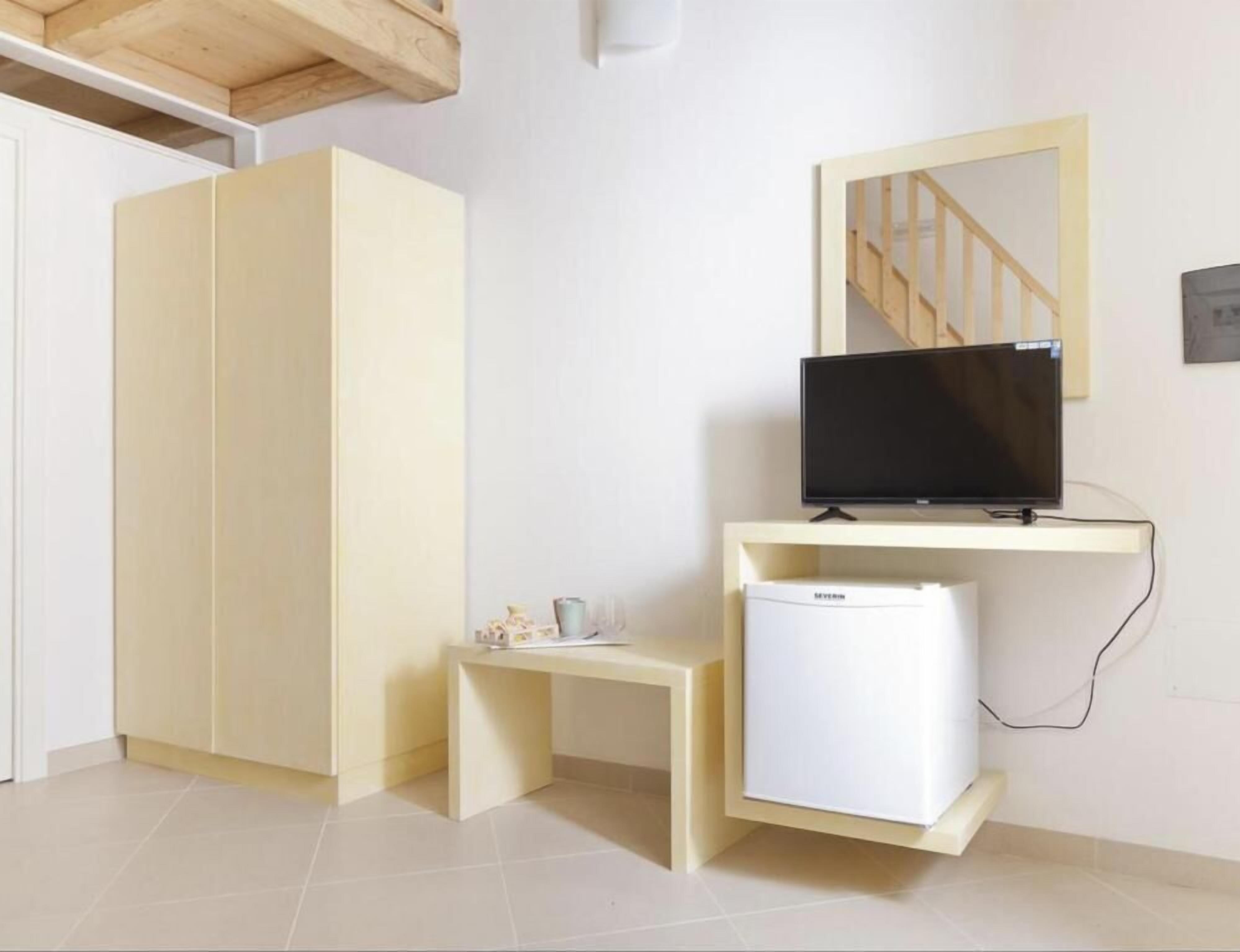 Una habitación con armario, un escritorio pequeño con televisor y un refrigerador.