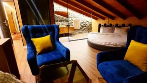 Ein Schlafzimmer mit einem Bett, zwei blauen Sesseln mit gelben Kissen, Holzboden und einer Steinwand im Hintergrund.