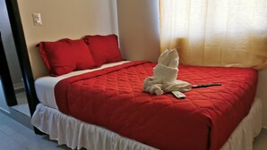 Een net opgemaakt bed met een rode deken en witte kussens, een afstandsbediening en een witte handdoek op het bed.