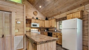 A wooden cabin kitchen with a central island, wooden cabinets, a white refrigerator, a microwave, a stove, and a dishwasher. - Bear cabin. This modern log cabin with HOT TUB is a large studio with a spectacular king size bed! (Tellico Plains)