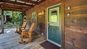 A wooden cabin with a green door, a porch with wooden chairs, and a wooden deck. - Bear cabin. This modern log cabin with HOT TUB is a large studio with a spectacular king size bed! (Tellico Plains)
