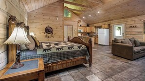 A cozy log cabin interior with a wooden bed, a sofa, a dining area, and a kitchen. - Bear cabin. This modern log cabin with HOT TUB is a large studio with a spectacular king size bed! (Tellico Plains)