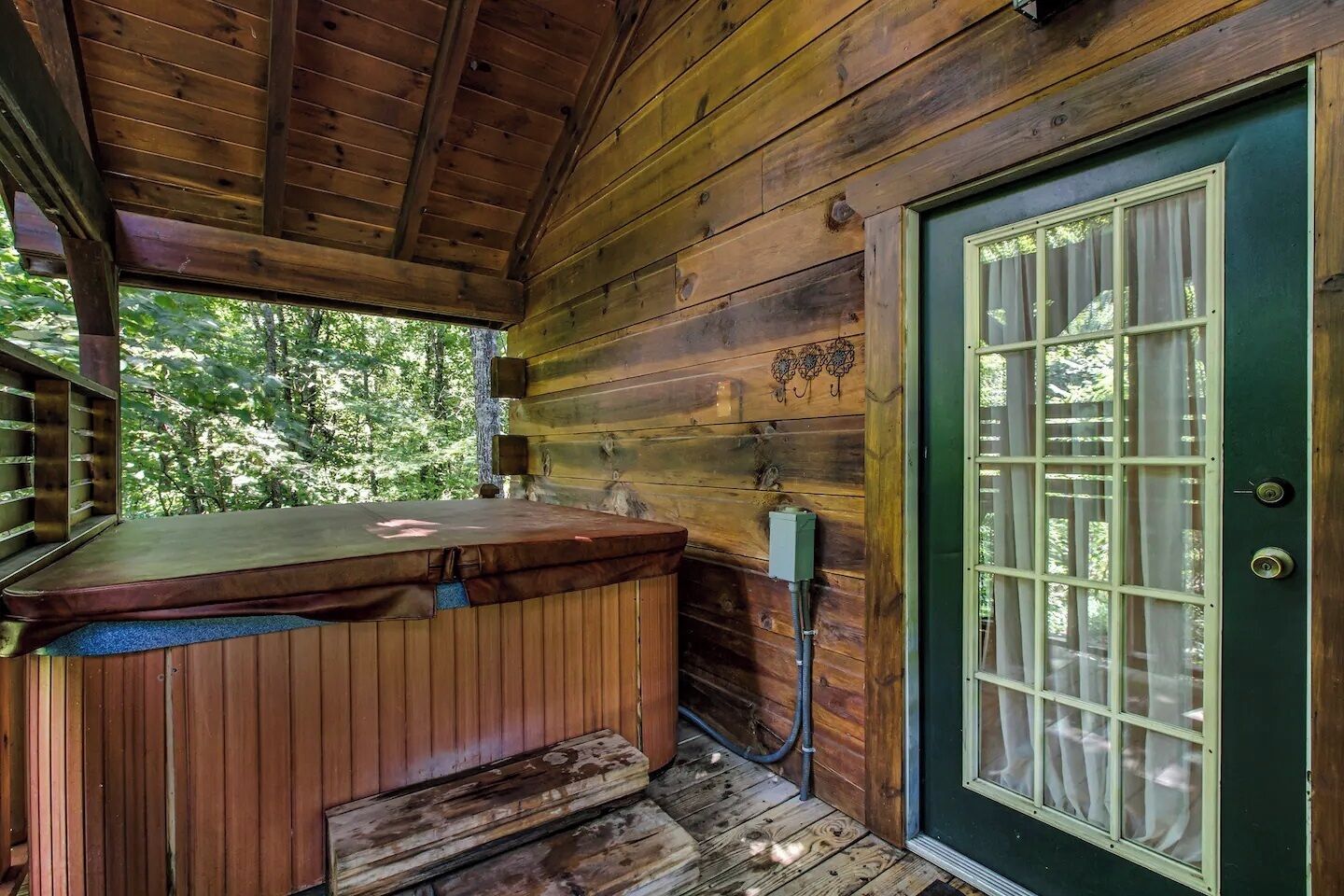 A wooden cabin with a hot tub, a door with glass panels, and a wooden deck.