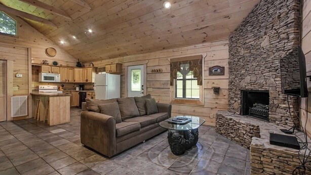 A cozy cabin interior with a stone fireplace, wooden ceiling, and a kitchenette. - Bear cabin. This modern log cabin with HOT TUB is a large studio with a spectacular king size bed! (Tellico Plains)