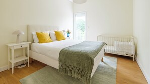 A bedroom with a bed, bedside table, lamp, and a crib.