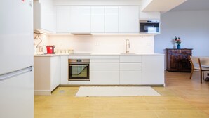 A modern kitchen with white cabinetry, a built-in oven, a microwave, and a wooden cabinet with a vase.