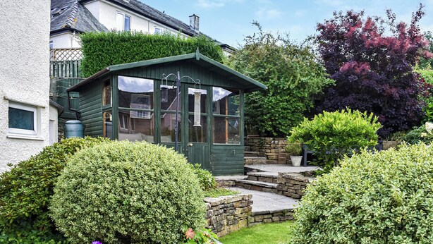 A green conservatory with a stone staircase leading up to it, surrounded by well-maintained hedges and a variety of plants. - 3 bedroom accommodation in Keswick (Keswick)