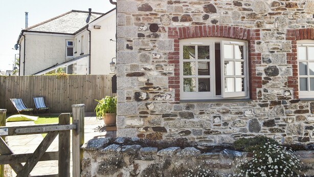 A stone building with a window and a door, a wooden fence, and a potted plant. - 2 bedroom accommodation in Par, near Fowey (Par, near Fowey)