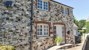 A stone building with a white door, windows, and a satellite dish. - 2 bedroom accommodation in Par, near Fowey (Par, near Fowey)