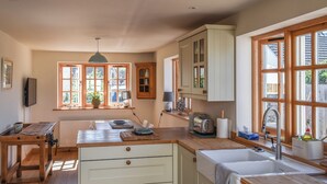 A kitchen with wooden cabinets, a sink, and a window with multiple panes. - 2 bedroom accommodation in Par, near Fowey (Par, near Fowey)