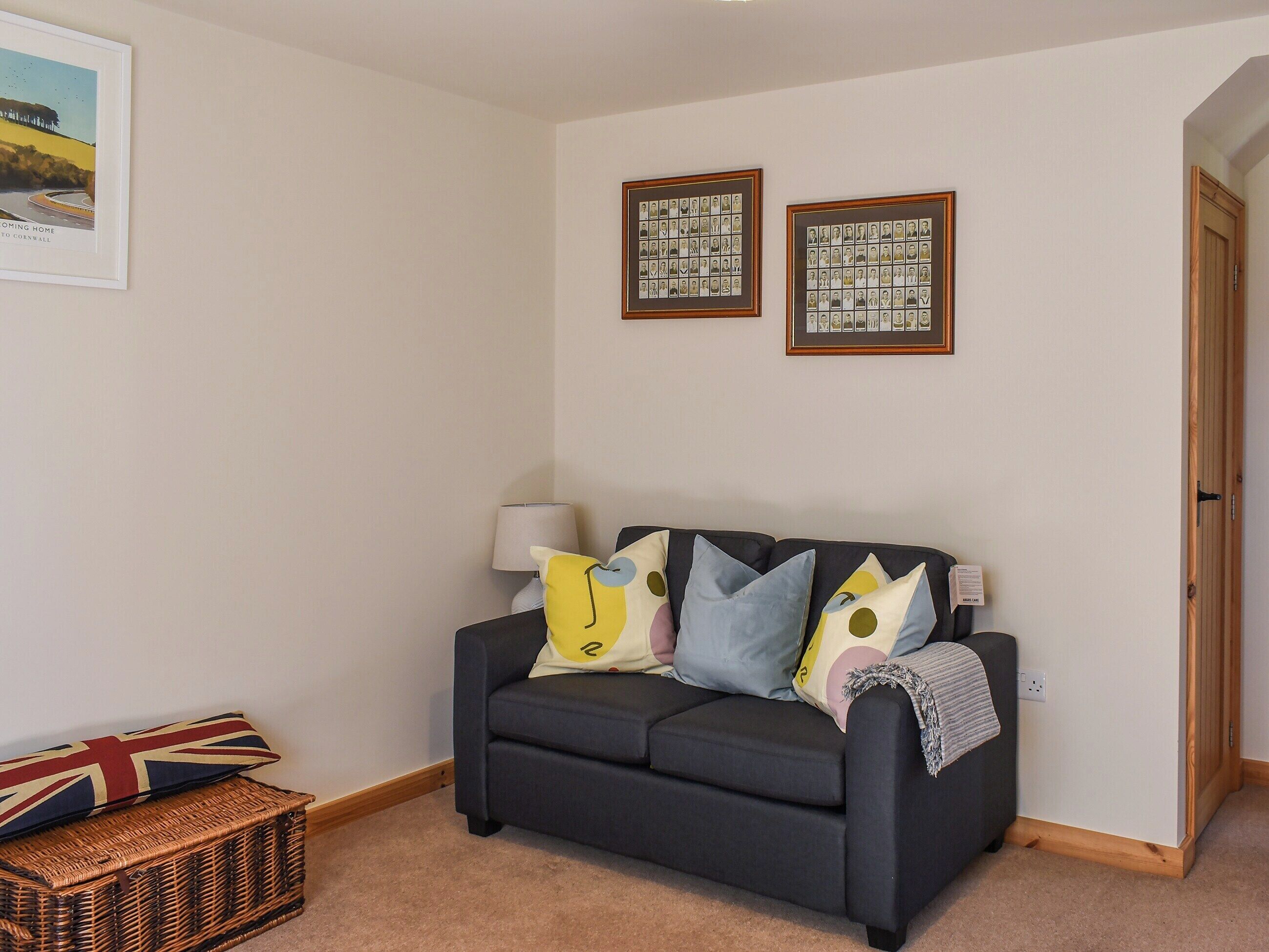 A living room with a dark grey sofa, a wicker basket, and two framed photographs on the wall.