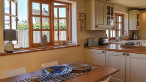 A kitchen with wooden cabinets, a dining table with chairs, and a window with a view of greenery. - 2 bedroom accommodation in Par, near Fowey (Par, near Fowey)