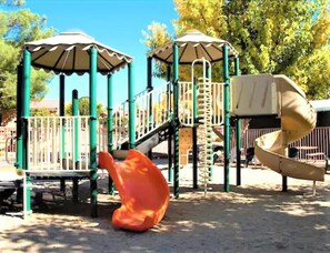 Kids can climb, slide, and play in the shaded playground surrounded by trees.